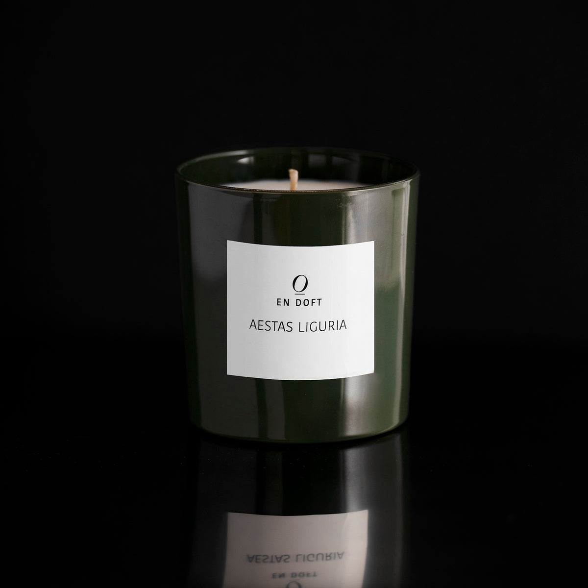 AESTAS LIGURIA scented candle by En Doft in a dark green glass vessel with a white label, on a black reflective surface.