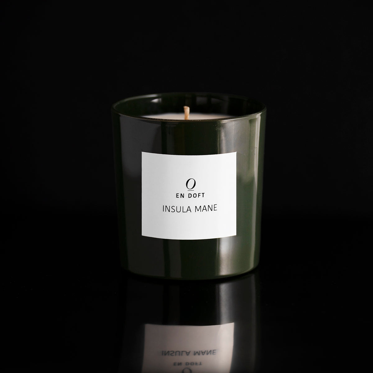 INSULA MANE scented candle by En Doft in a dark green glass vessel with a white label, on a black reflective surface.